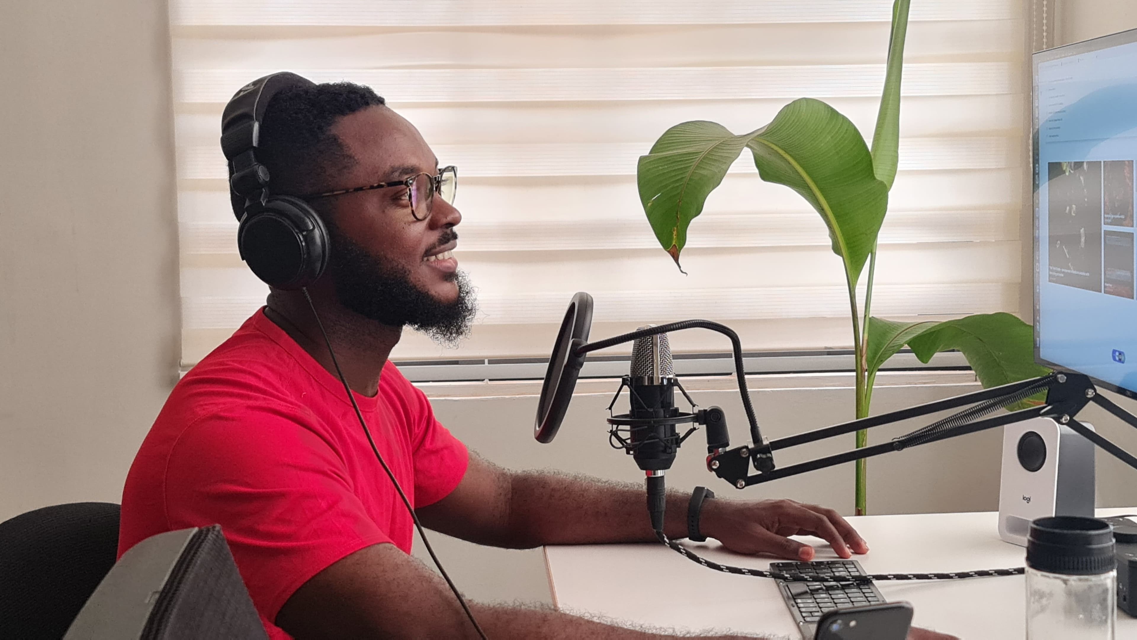 A podcaster wearing headphones working at a computer with editing software open.